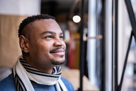 Man wearing a scarf smiles as he looks out a window