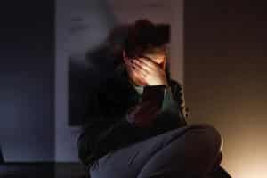 A woman seated in the dark shields her eyes from her bright phone screen
