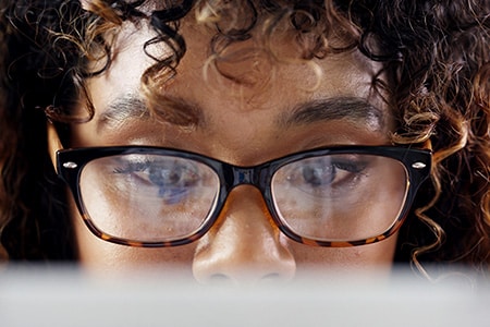 Closeup of a focused woman wearing glasses looking at laptop screen