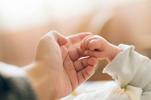 Close-up shot of an adult hand holding an infant's hand